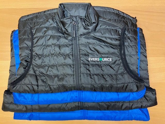 A black vest and a blue vest are stacked on top of each other on a table.