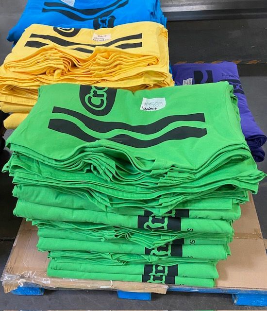 A stack of green and yellow crayon t-shirts on a pallet