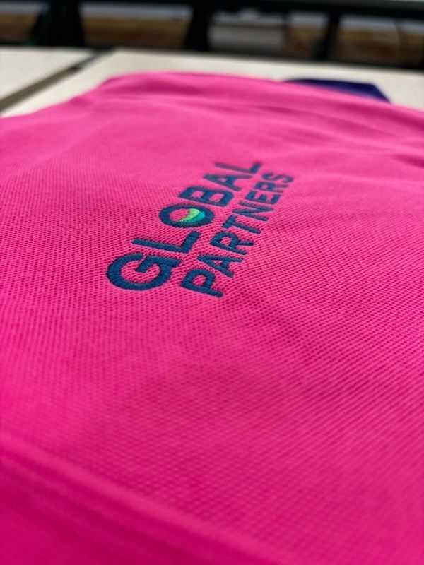A close up of a pink shirt with the words `` global partners '' embroidered on it.