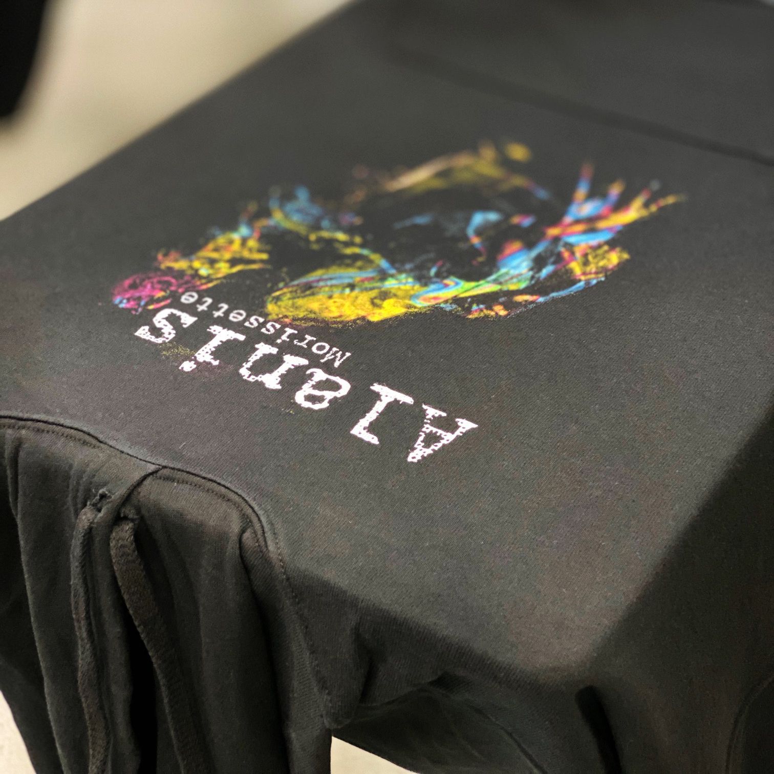 A black t-shirt with a colorful design on it is sitting on a table.