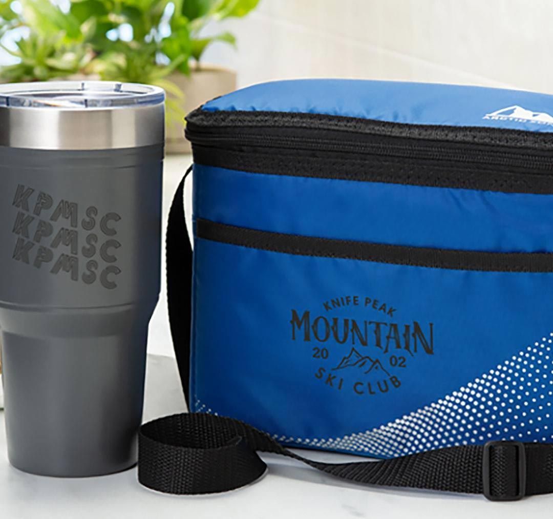 A blue bag that says mountain sits next to a tumbler