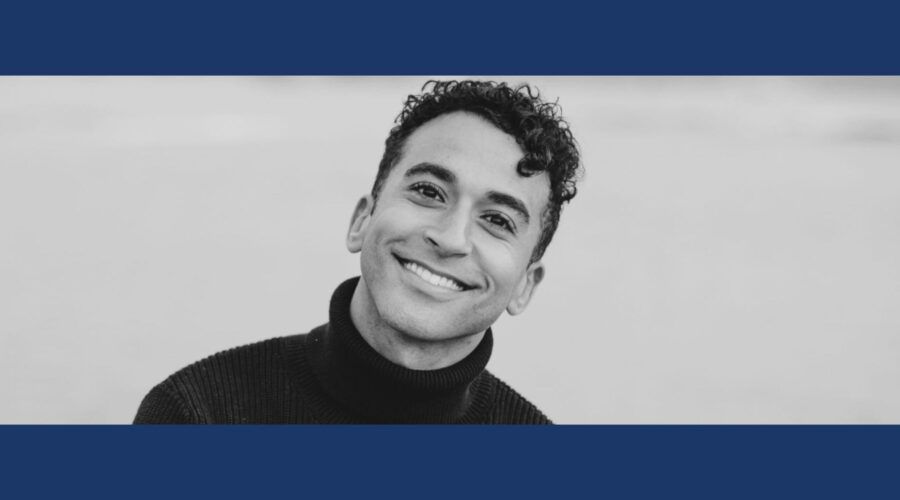 Smiling person in black turtleneck, headshot in front of a neutral backdrop, black and white.