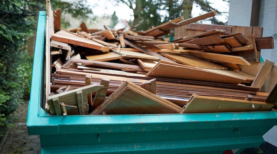 Green dumpster filled with wooden debris, possibly from construction or renovation.