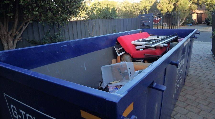 Blue dumpster filled with discarded items, including a red couch, outdoors.