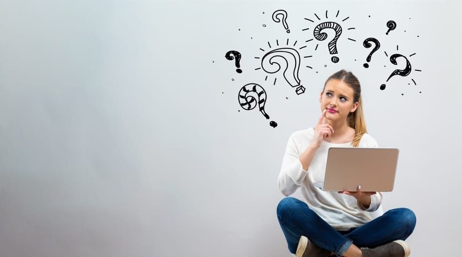 Woman sitting with laptop, pondering, question marks drawn overhead.