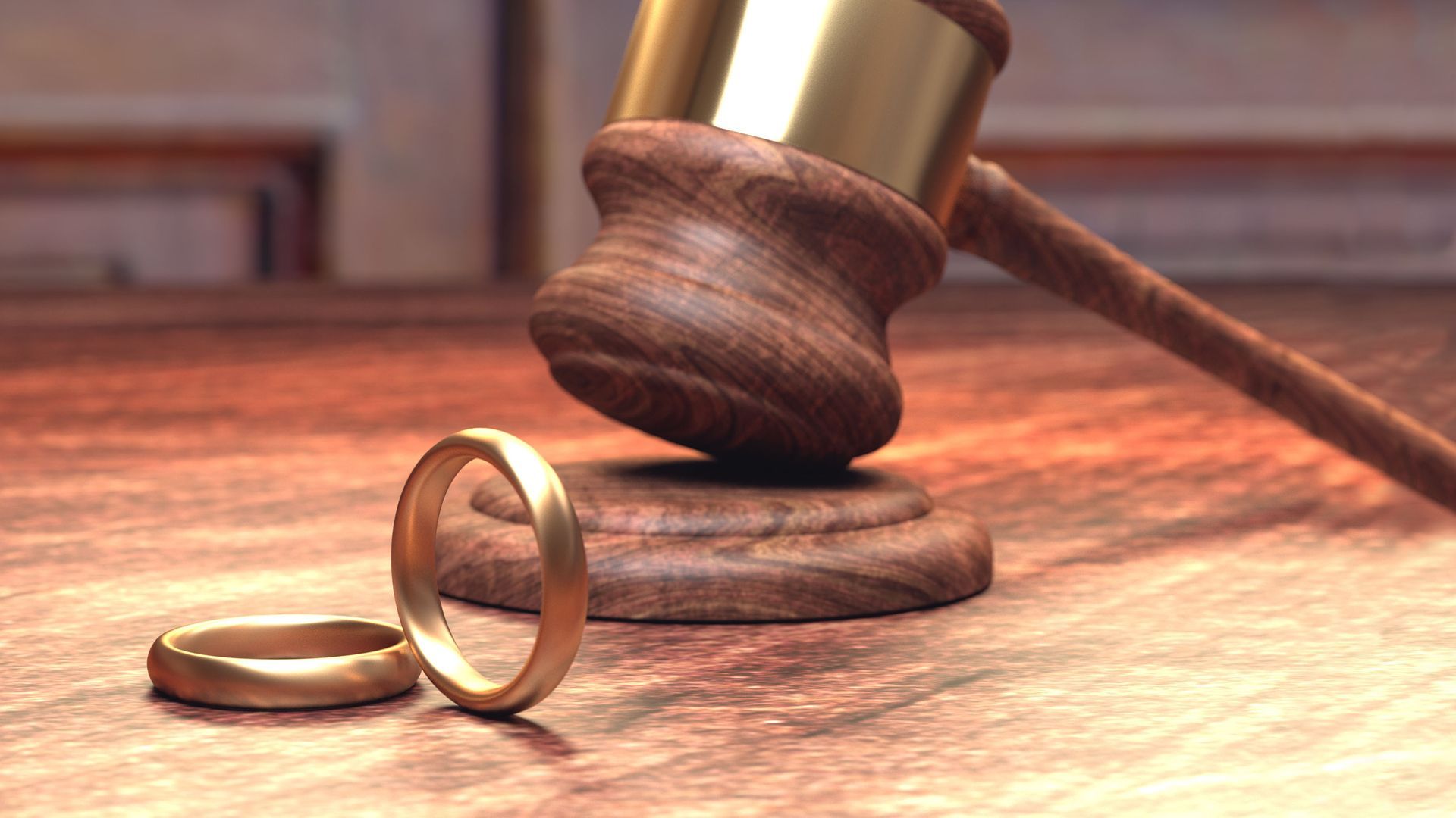 Two wedding rings are sitting on a wooden table next to a judge's gavel