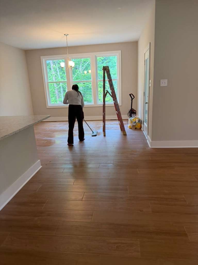 Person standing in a bright empty room with hardwood floors and a ladder near the windows