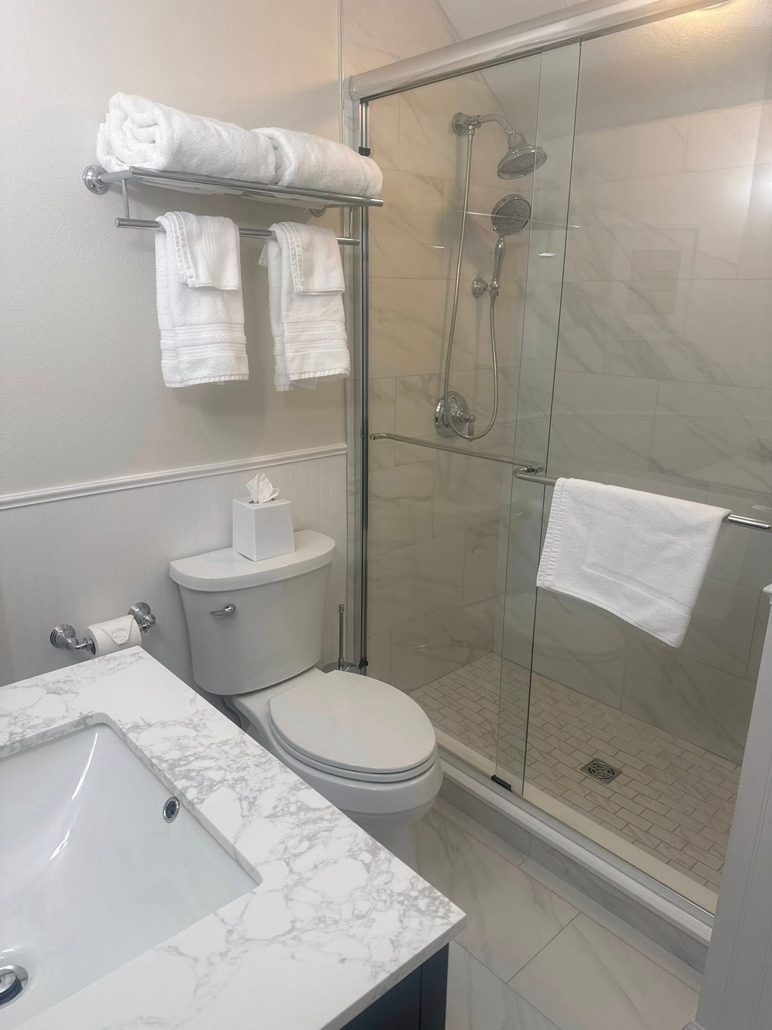 Modern bathroom with marble vanity, toilet, glass shower, and white towels