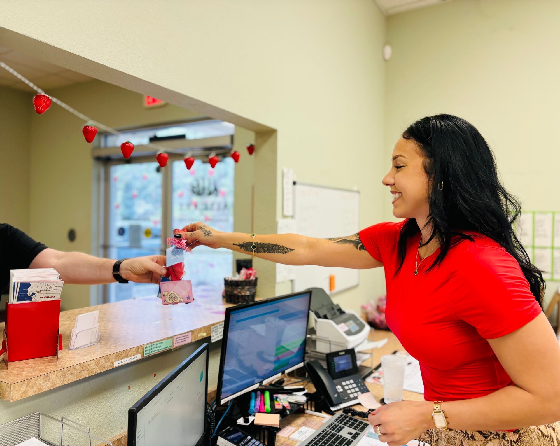 A woman in a red shirt is giving a card to a man at a counter.