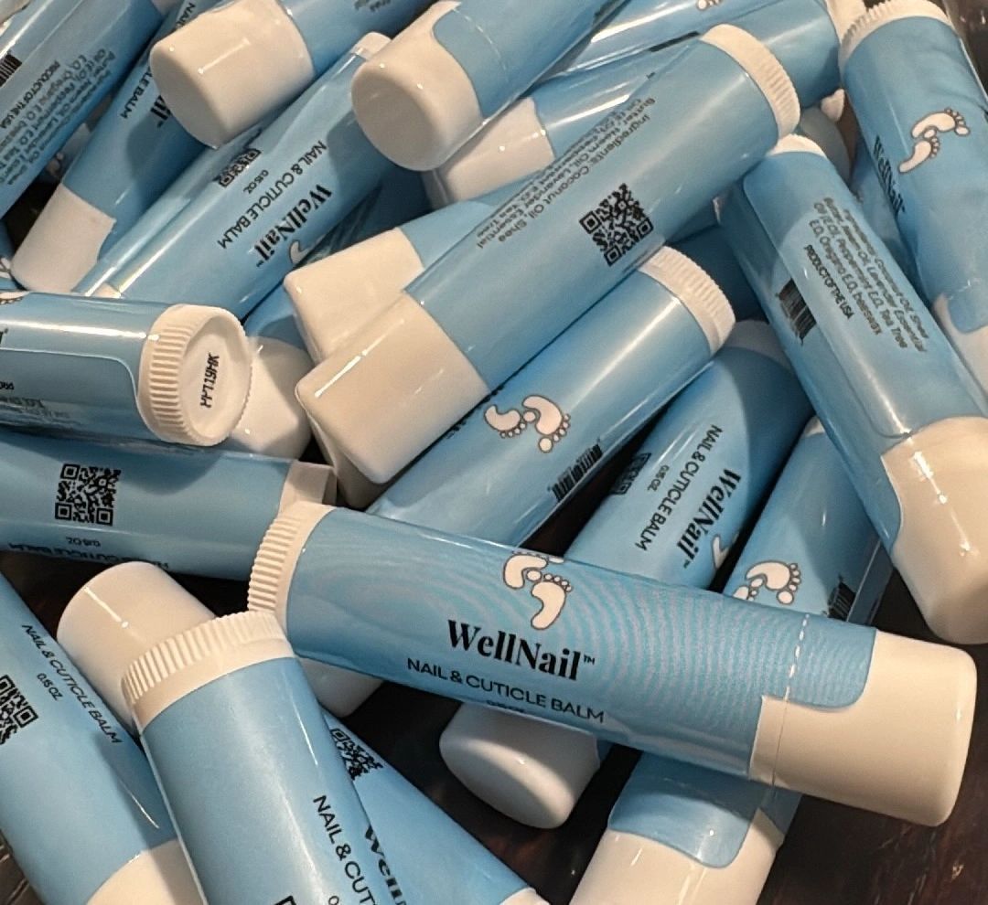 Pile of light blue WellNail cuticle balm tubes with white caps, and a foot logo.