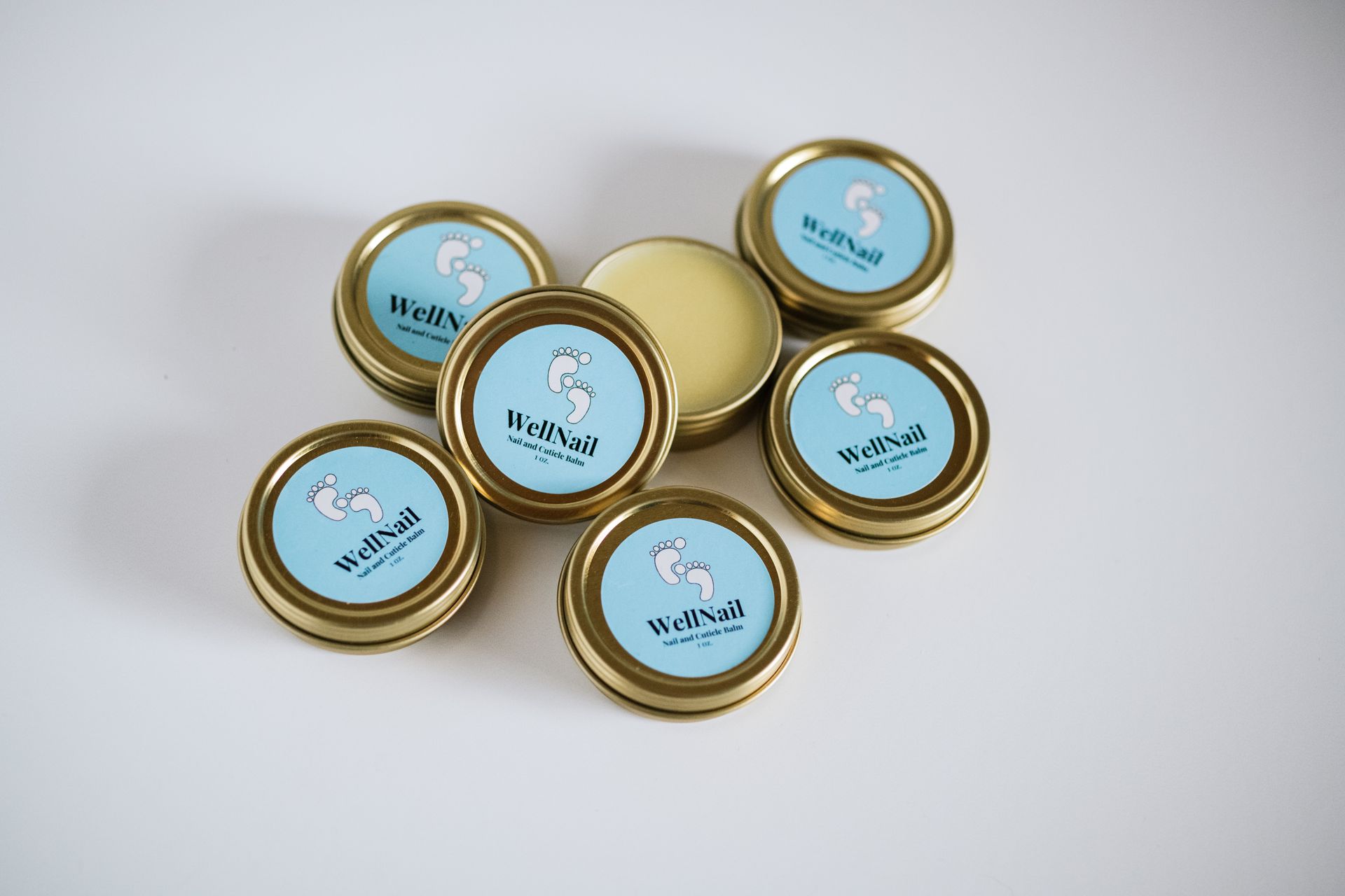 Seven gold-rimmed tins with a seahorse logo on a pale blue background; one is open, showing balm.