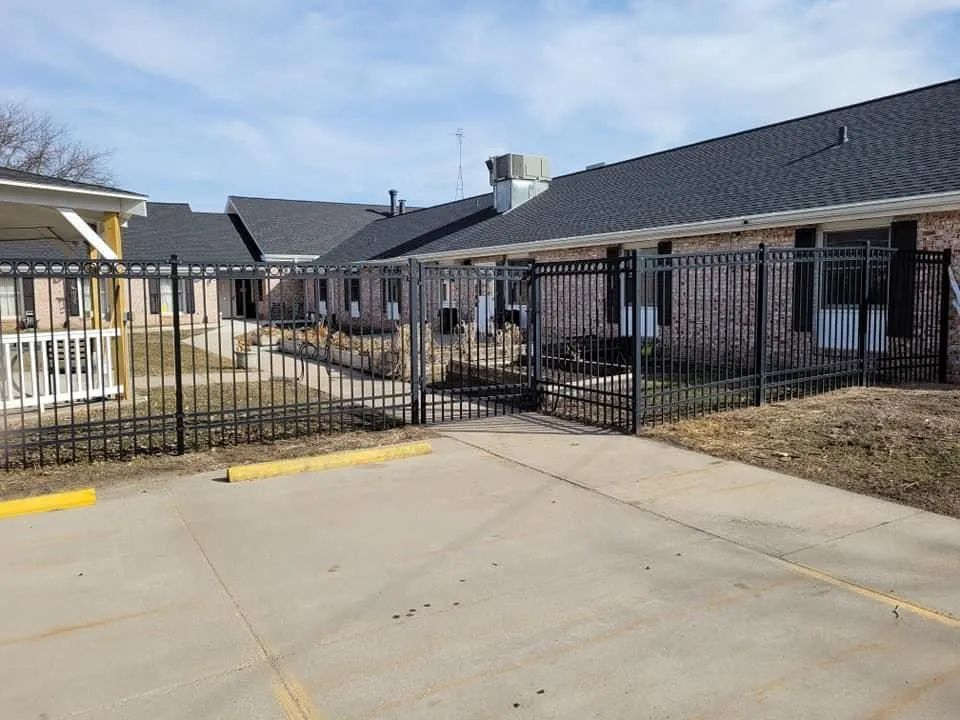 Black metal gate across a concrete driveway in front of single-story buildings.