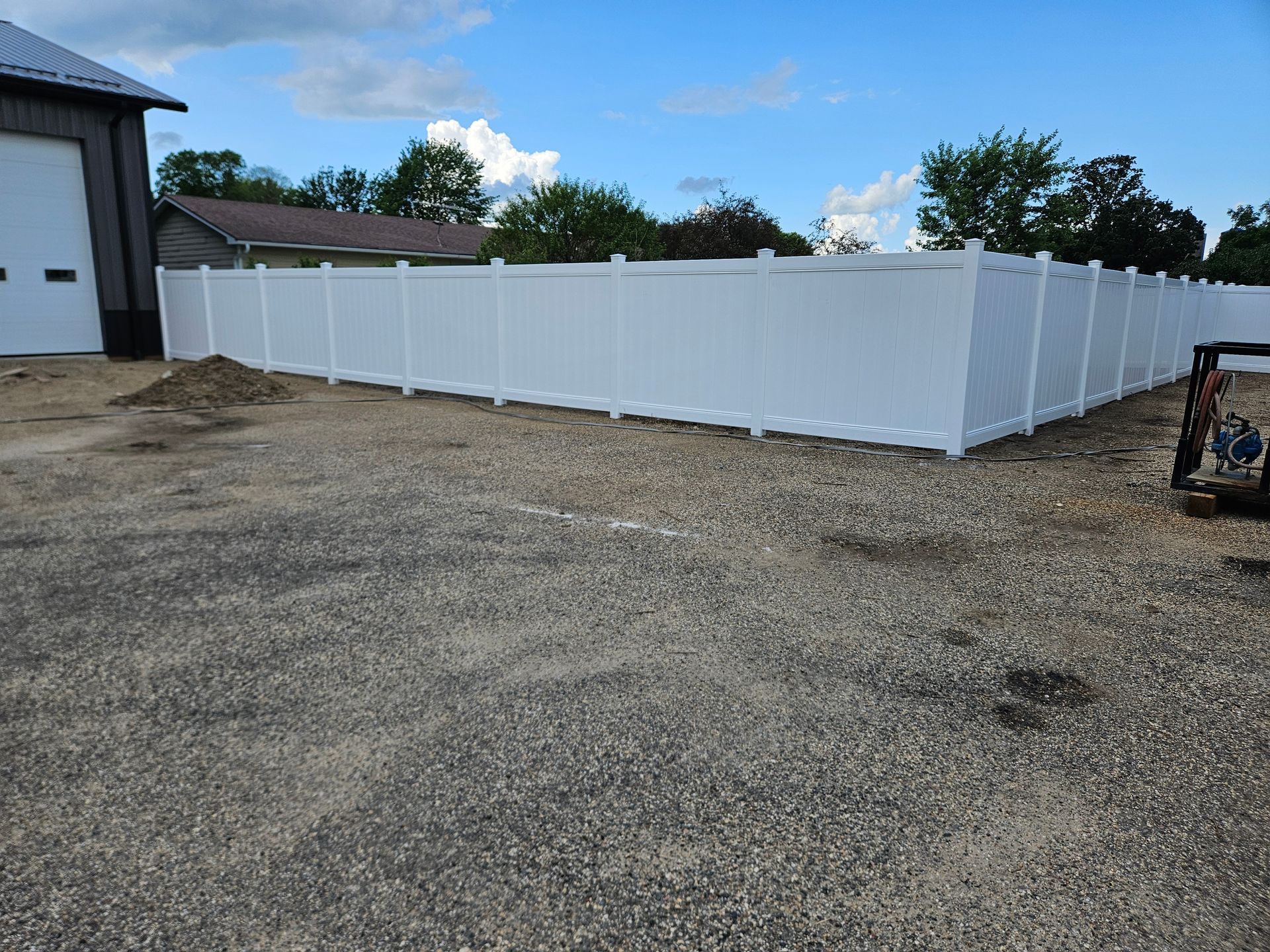 White vinyl fence enclosing a gravel yard beside a building on a clear day