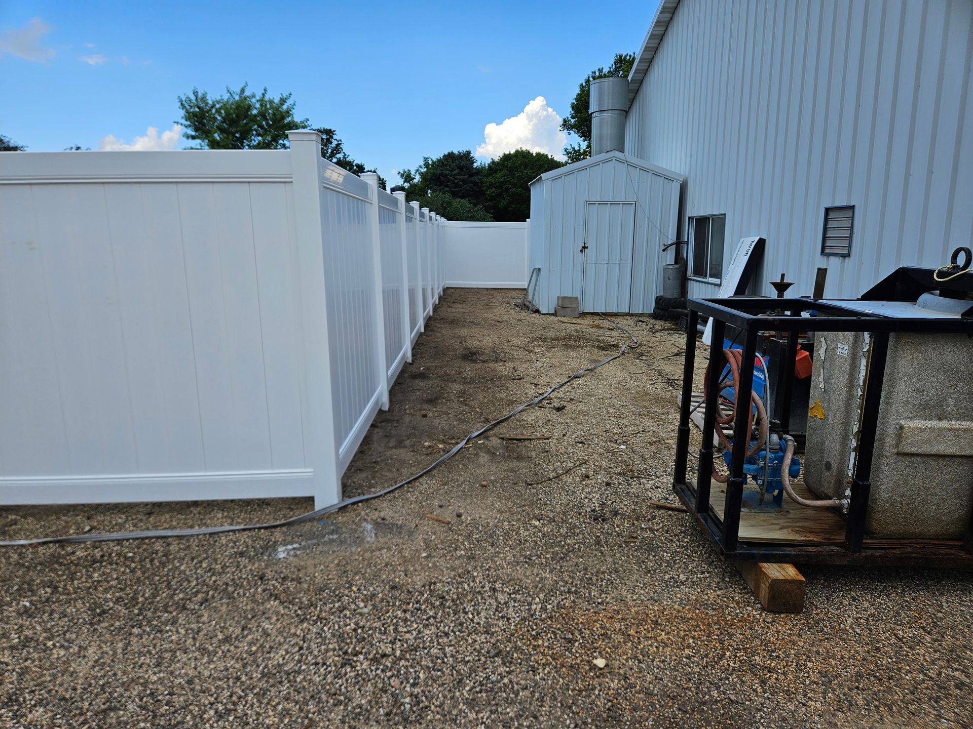 Gravel path between white fences leading to a small shed, with a metal table on the right.