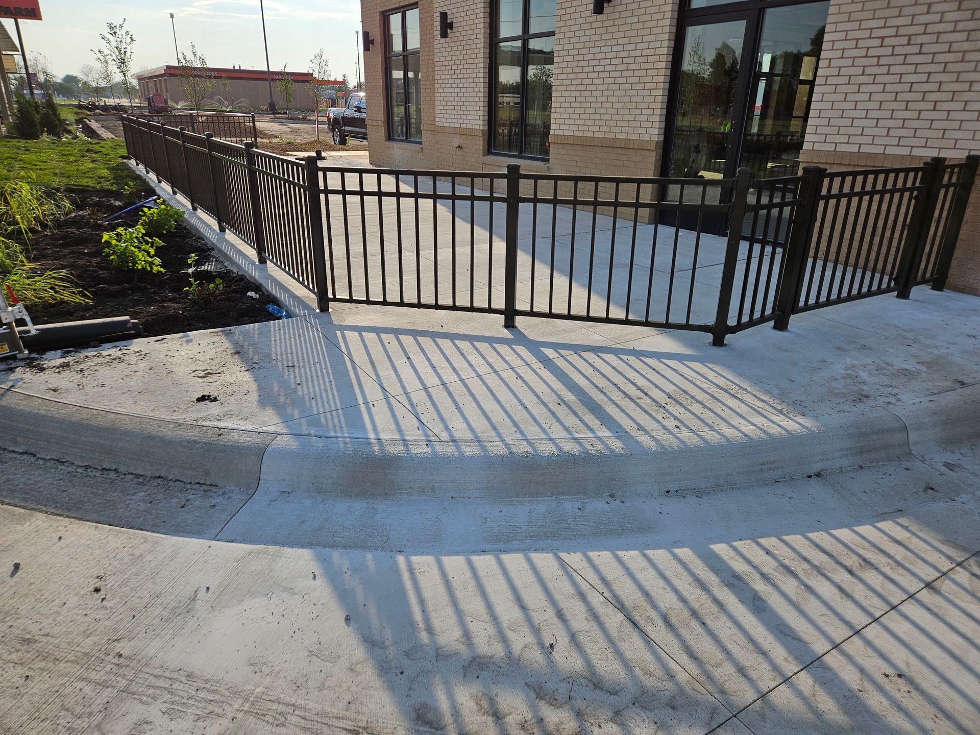 Black metal fence beside a building entrance with a concrete walkway and long morning shadows
