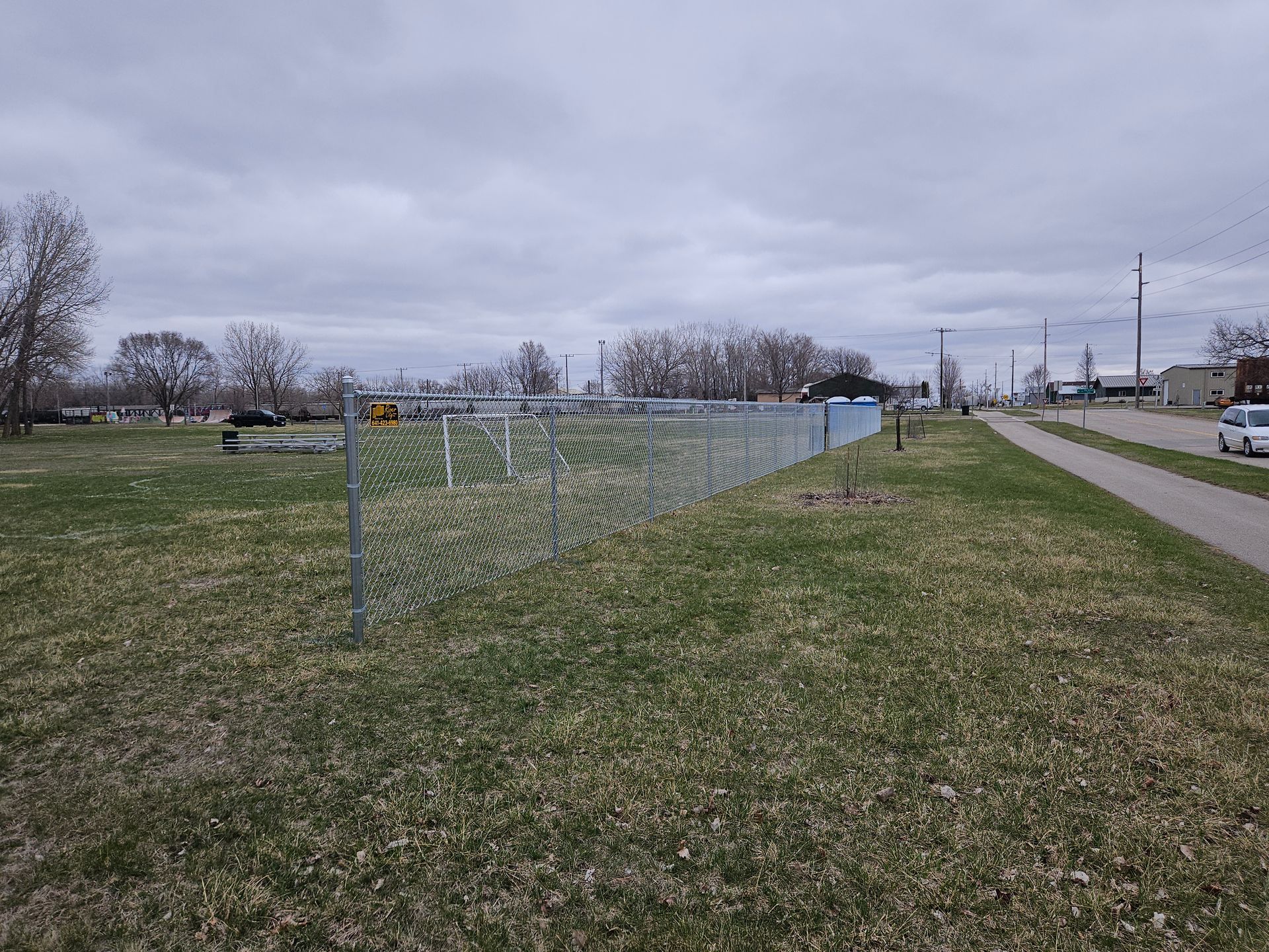 Chain-link fence along a grassy roadside with bare trees and overcast sky
