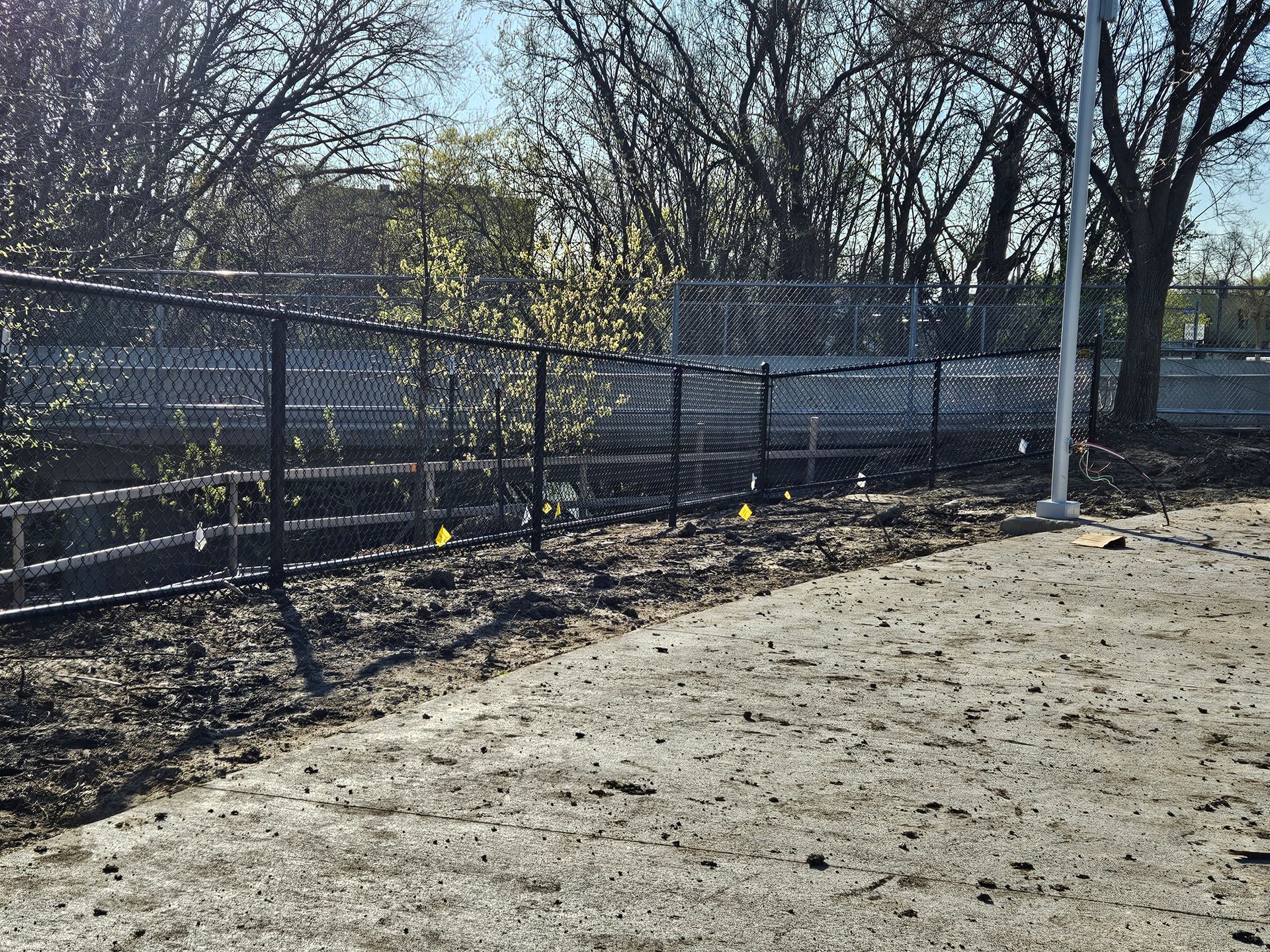 Chain-link fence beside a dirt path under leafless trees on a sunny day