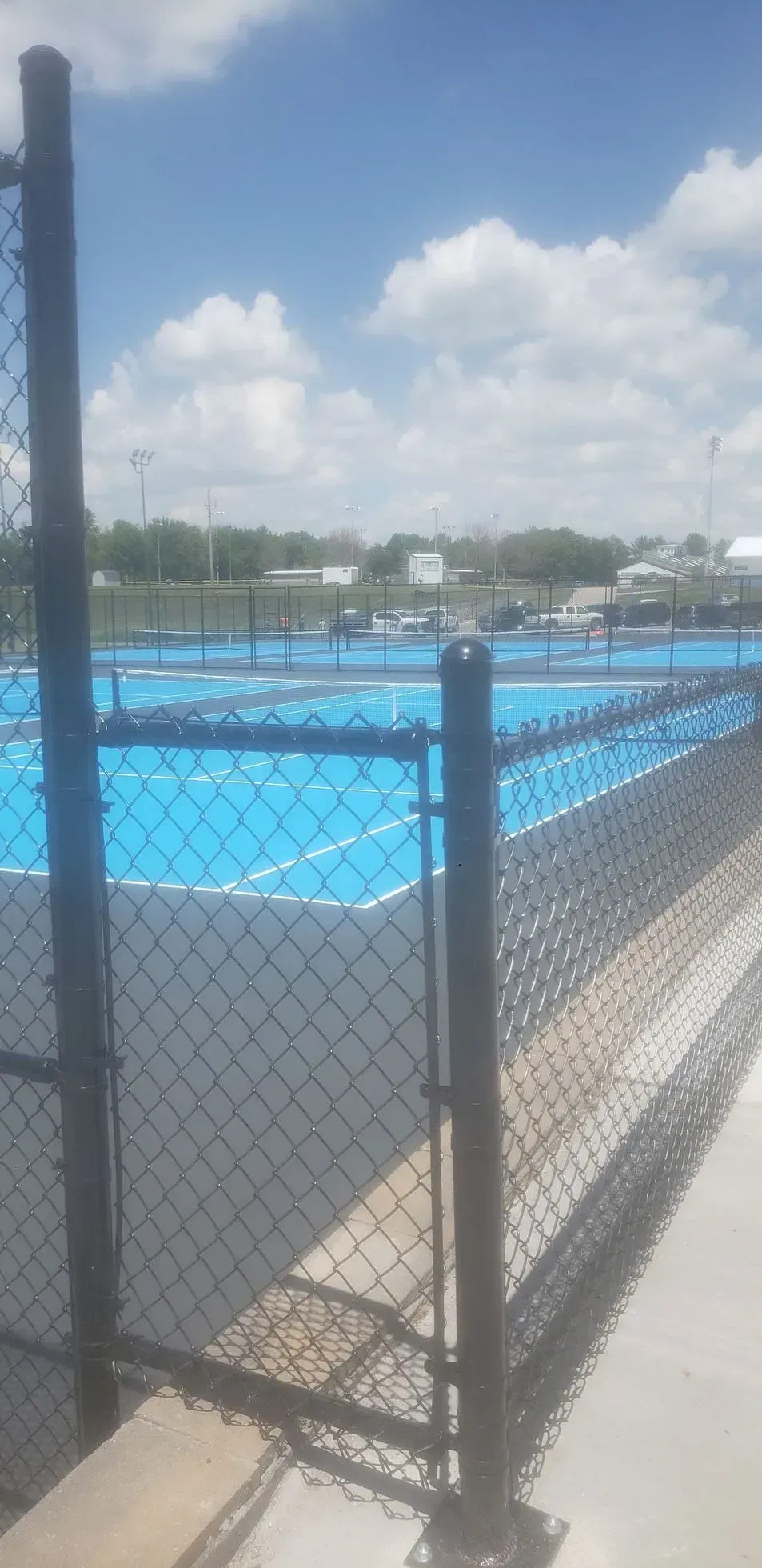 Blue outdoor swimming pool behind a chain-link fence under a partly cloudy sky