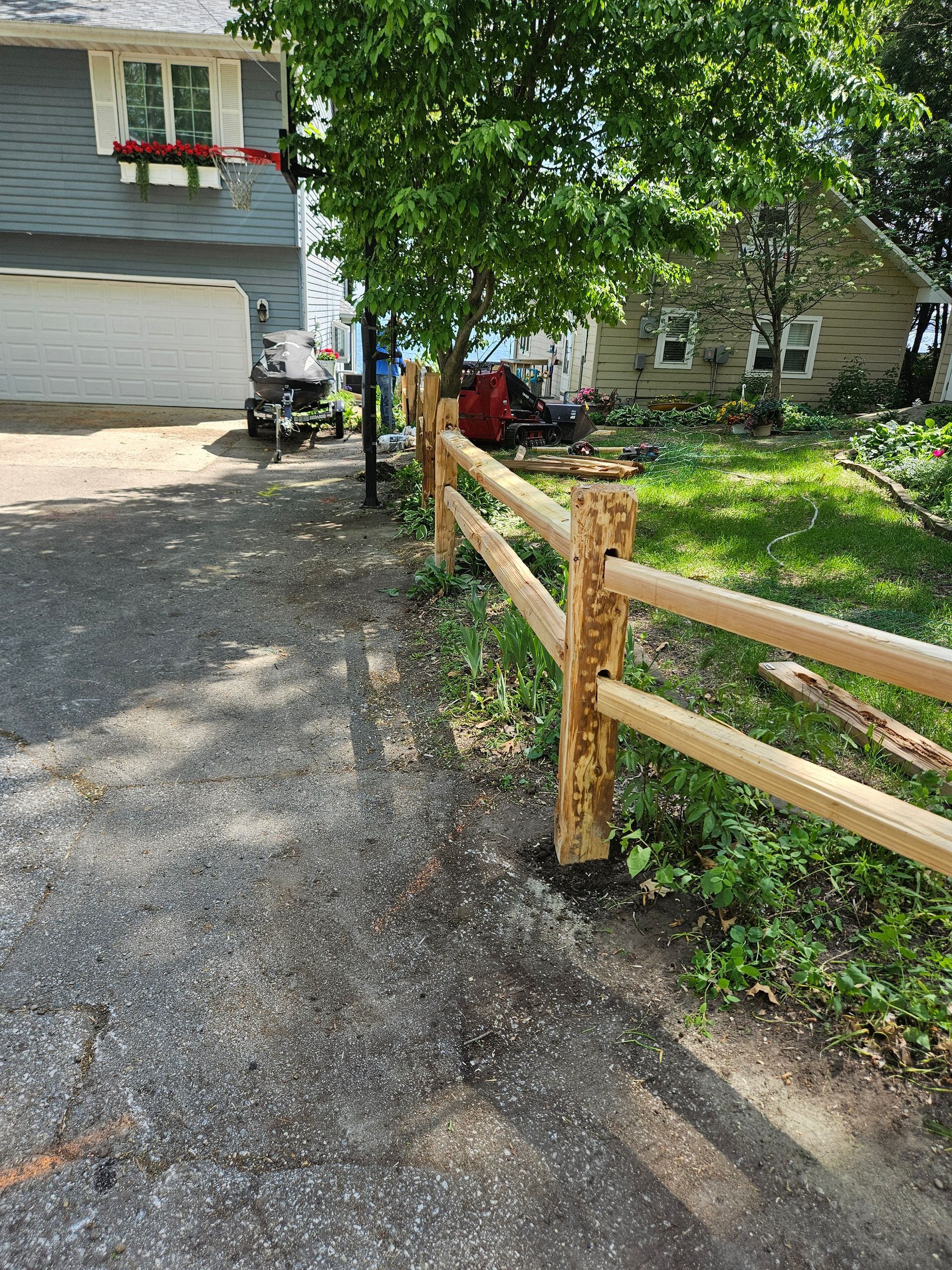 Gravel driveway beside a wooden fence, leading past a house and trees on a sunny day