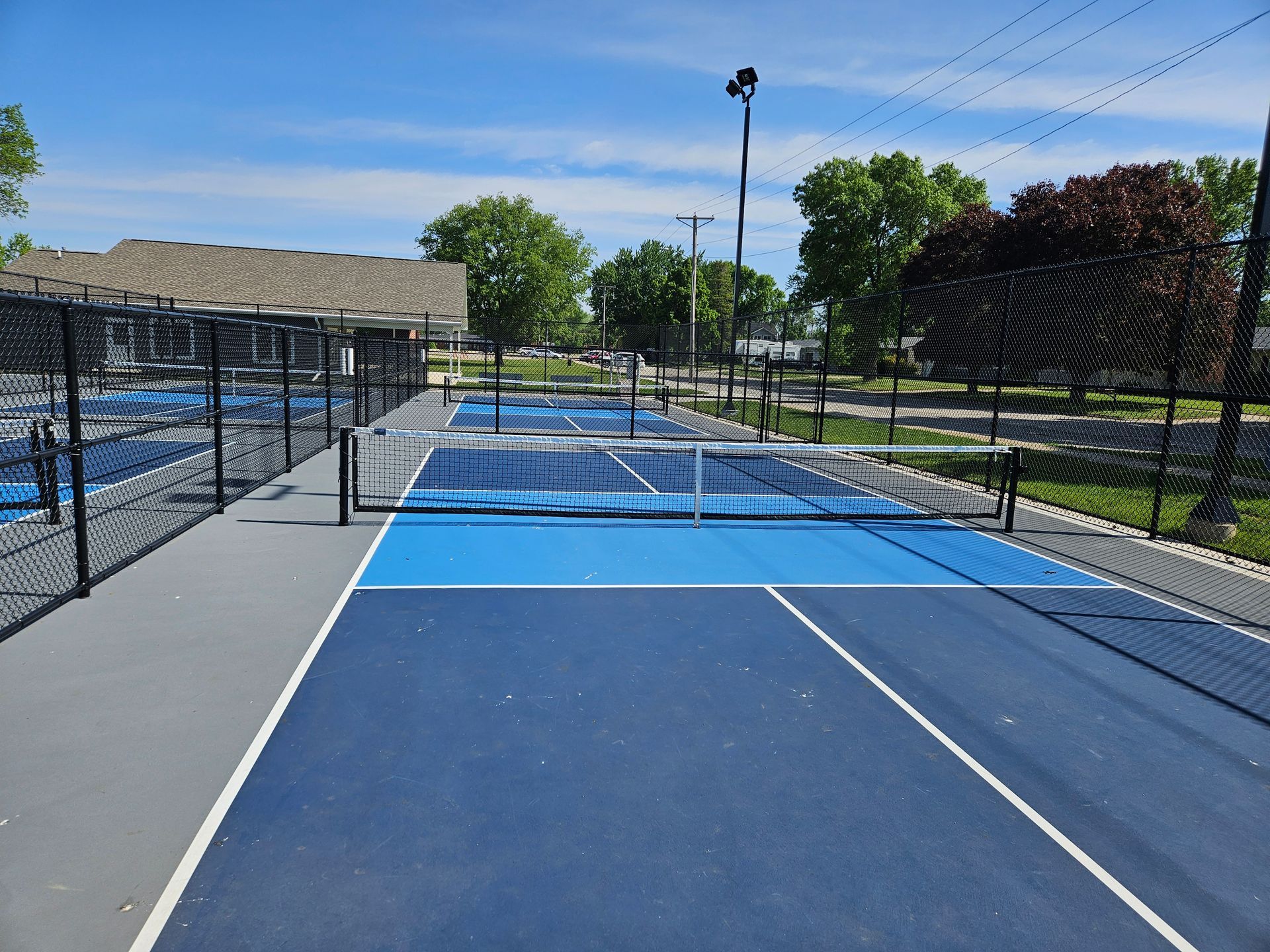 Outdoor blue tennis court with a net, fenced sides, and trees under a clear sky