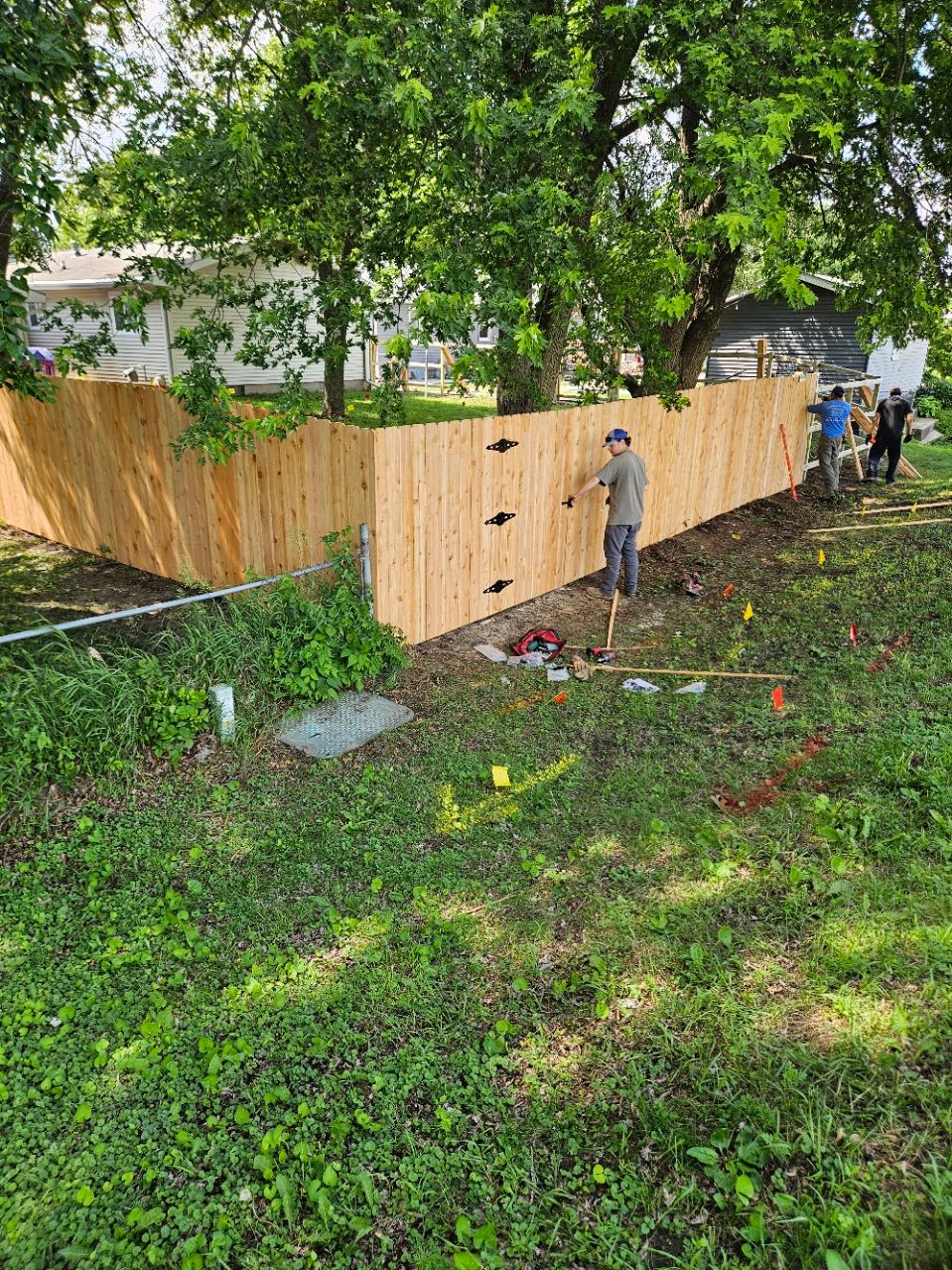 Wooden fence corner in a grassy yard, with a person standing near the fence and another near the right edge.