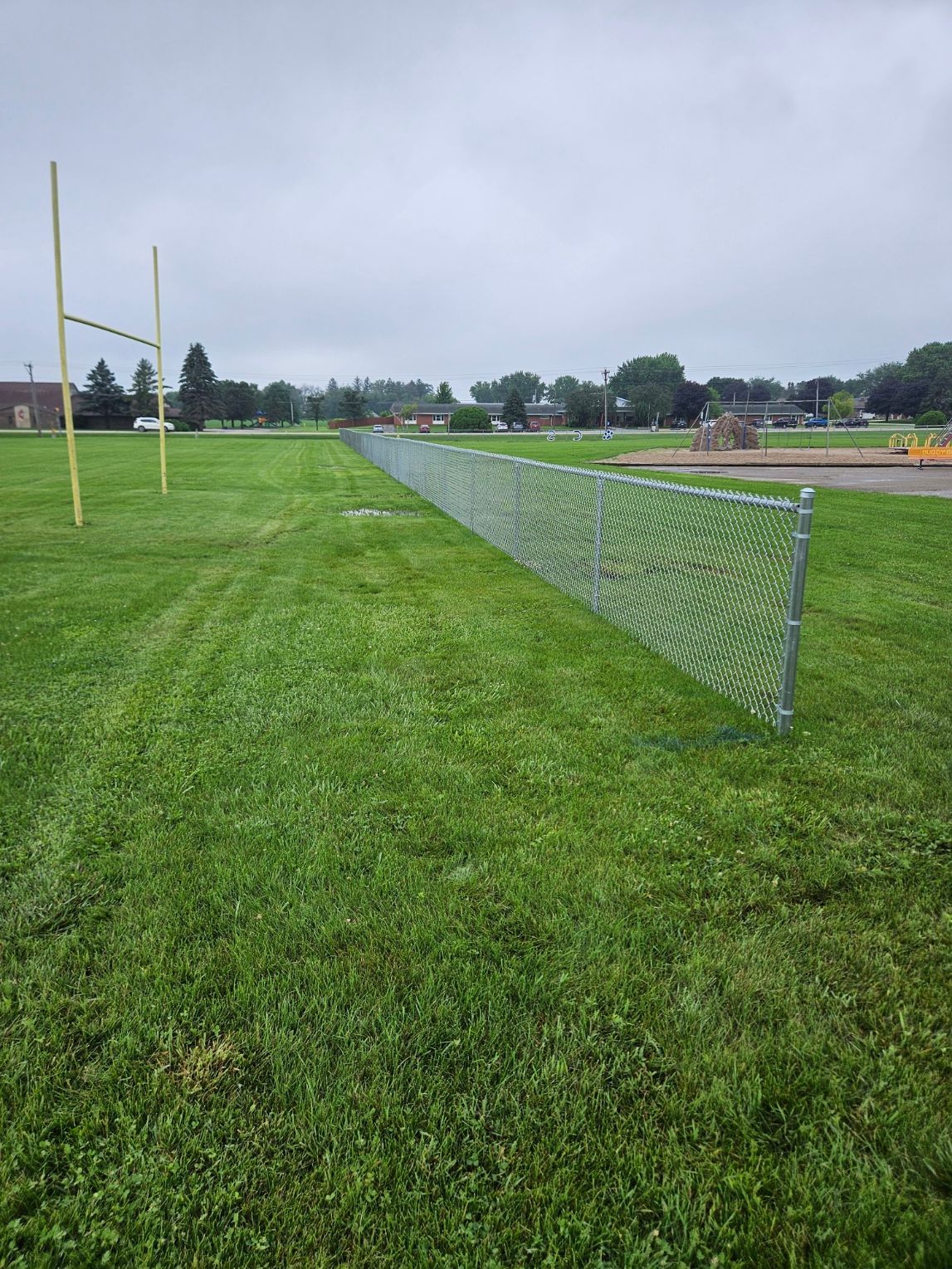 Chain-link fence along a grassy sports field under a cloudy sky