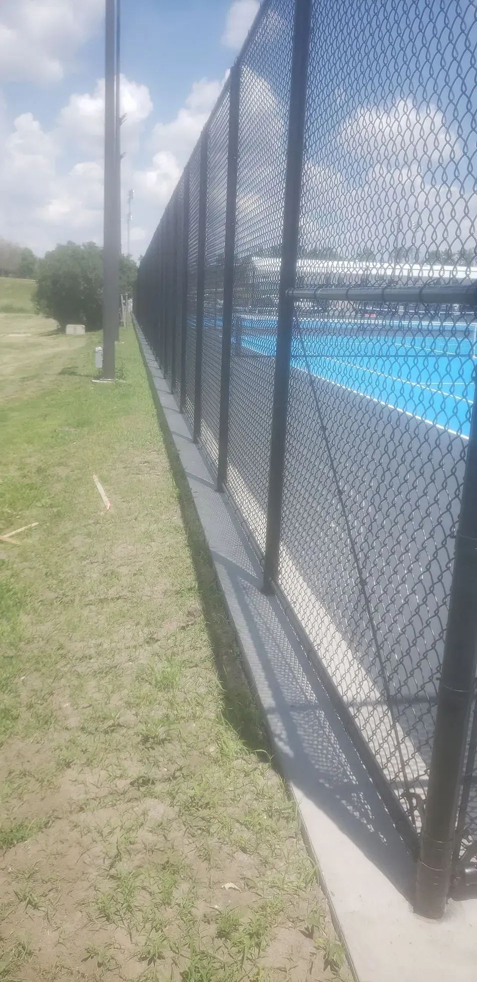 Chain-link fence beside a bright blue swimming pool on a sunny grassy lawn