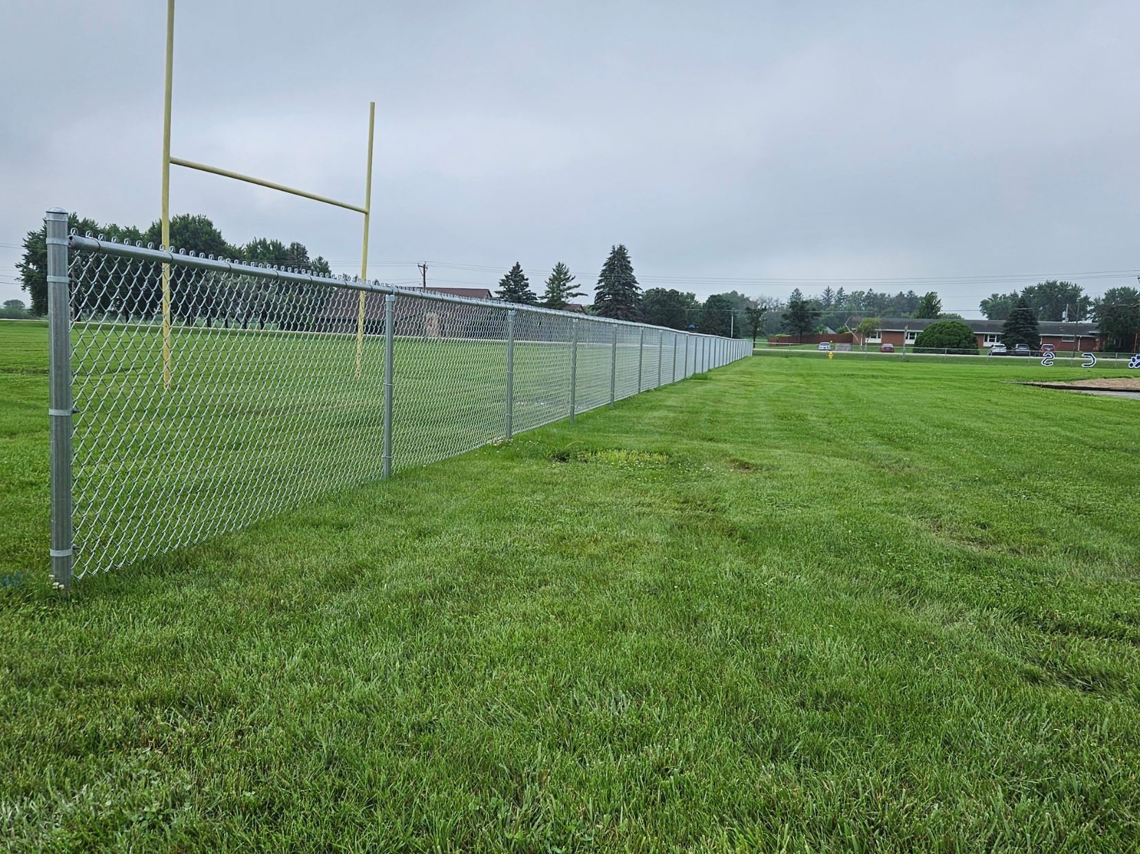 Grassy sports field with a chain-link fence and yellow goal posts under a cloudy sky