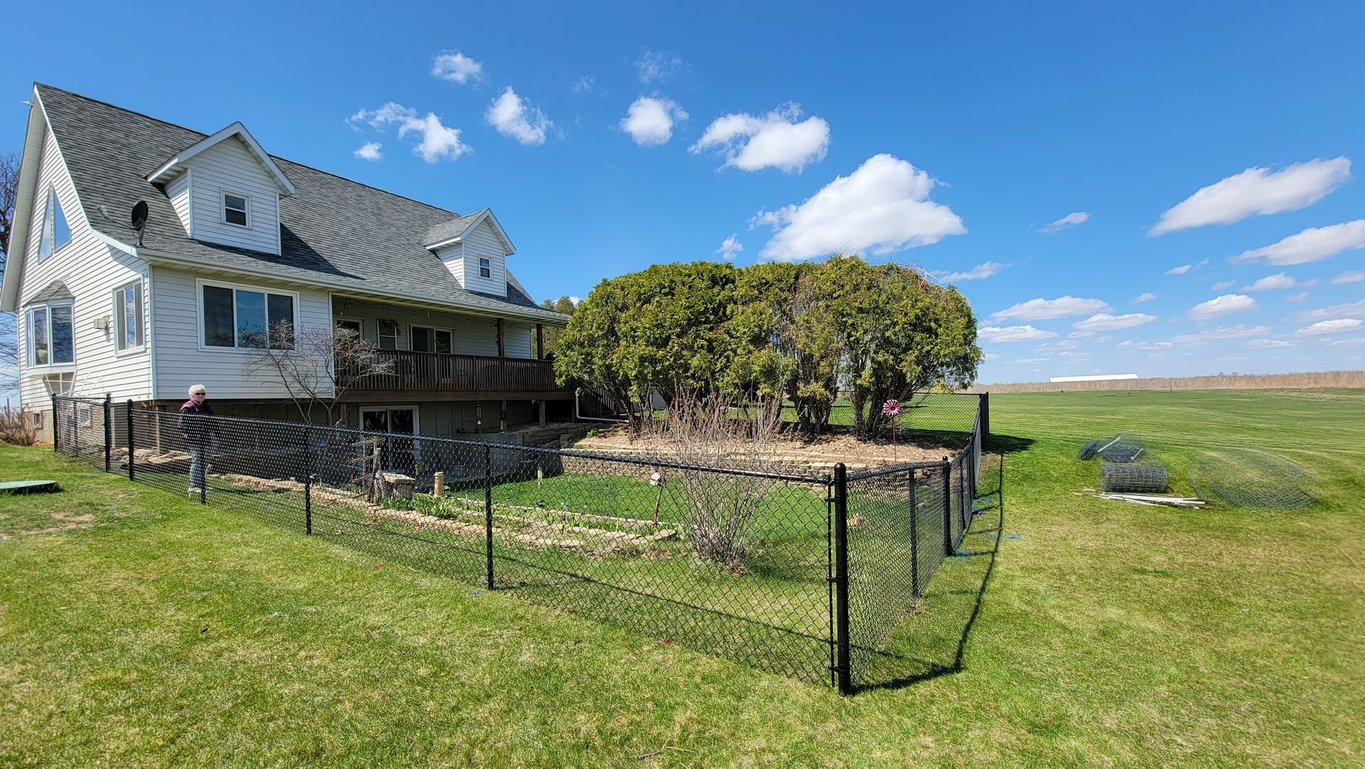 White farmhouse beside a fenced yard under a blue sky on a grassy rural lot