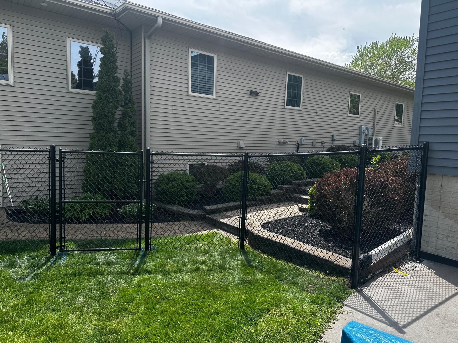 Black chain-link fence enclosing a narrow side yard beside a beige house and gray driveway.