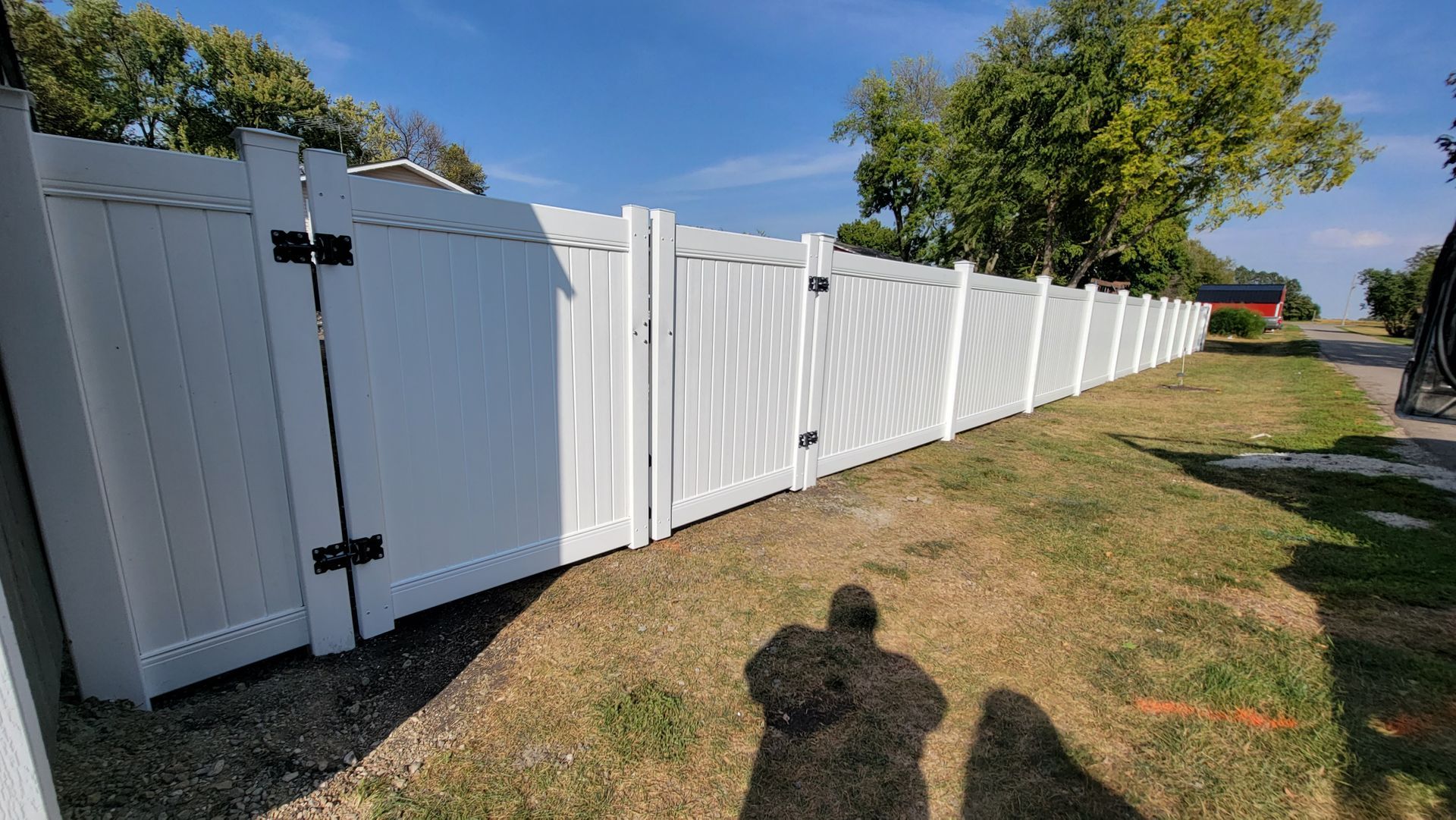 White vinyl fence and gate lining a grassy yard under a clear blue sky.