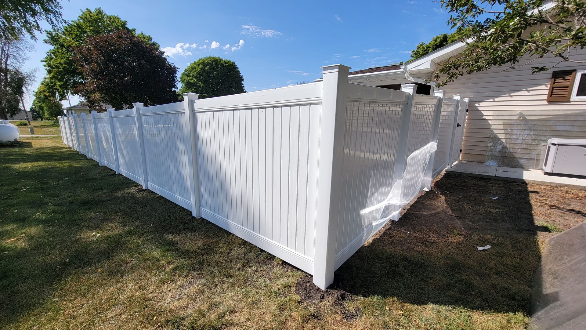 White vinyl privacy fence around a yard beside a house on a sunny day.