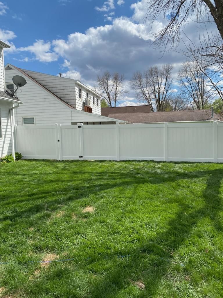 Backyard with green grass, white vinyl fence, and a cloudy blue sky behind a house.