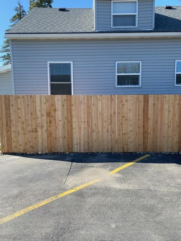 Wooden privacy fence across a parking lot in front of a gray house with a dormer window