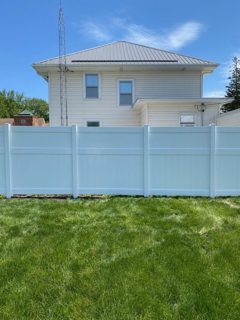 Light blue vinyl fence in front of a beige house with a gray roof and green lawn