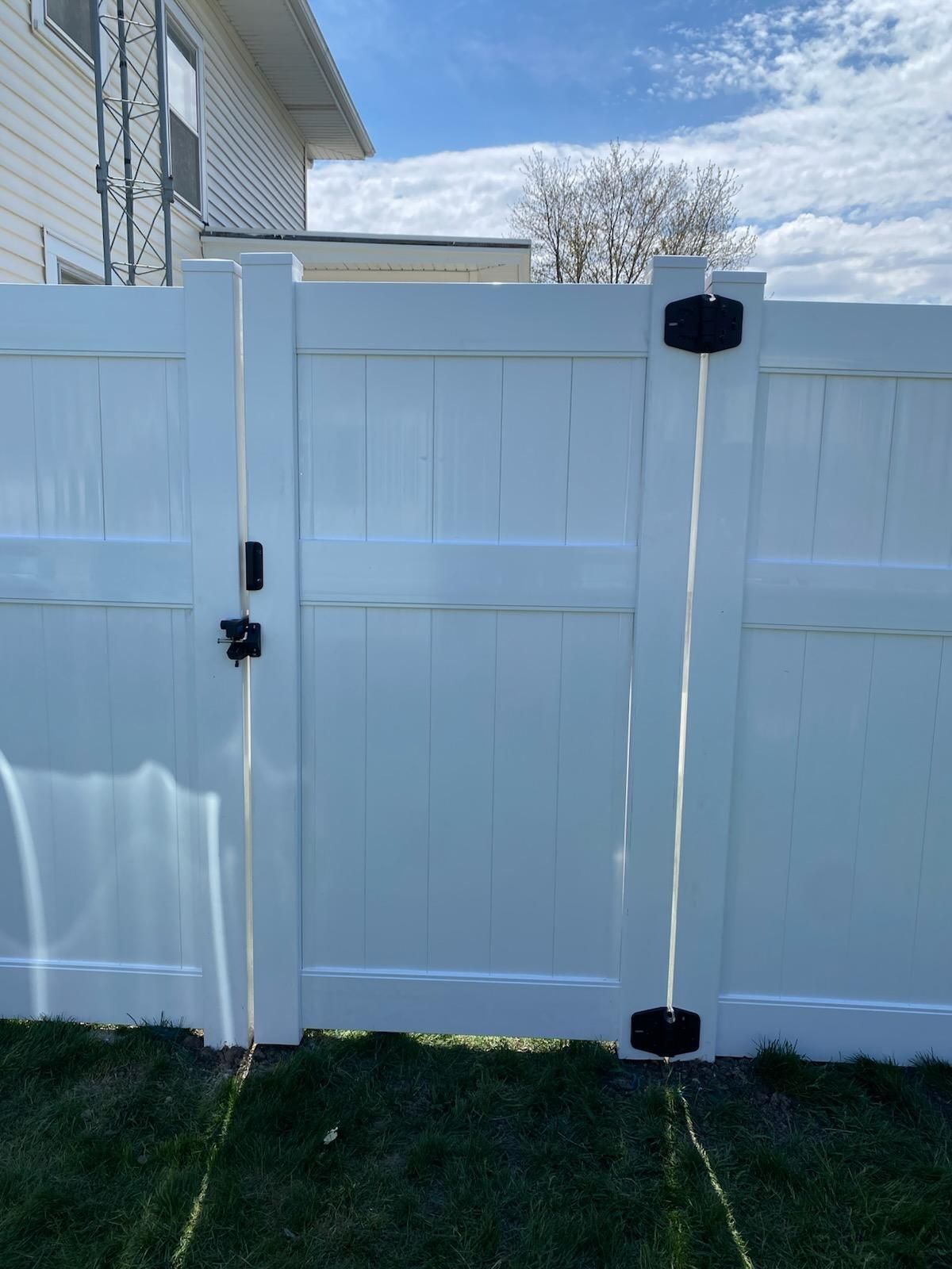 White vinyl backyard gate with black hinges and latch beside a house and grass lawn