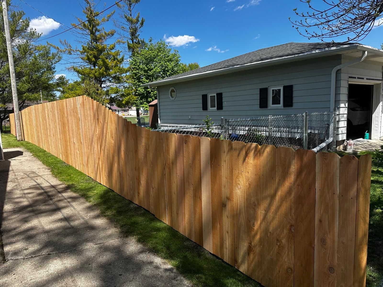 Wooden privacy fence along a narrow driveway beside a gray house under a blue sky