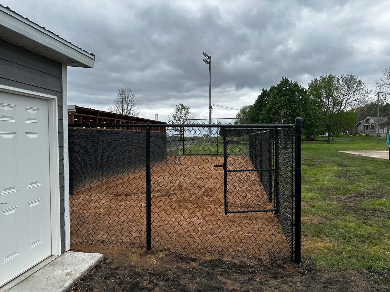 Chain-link fenced gravel area beside a garage under cloudy skies