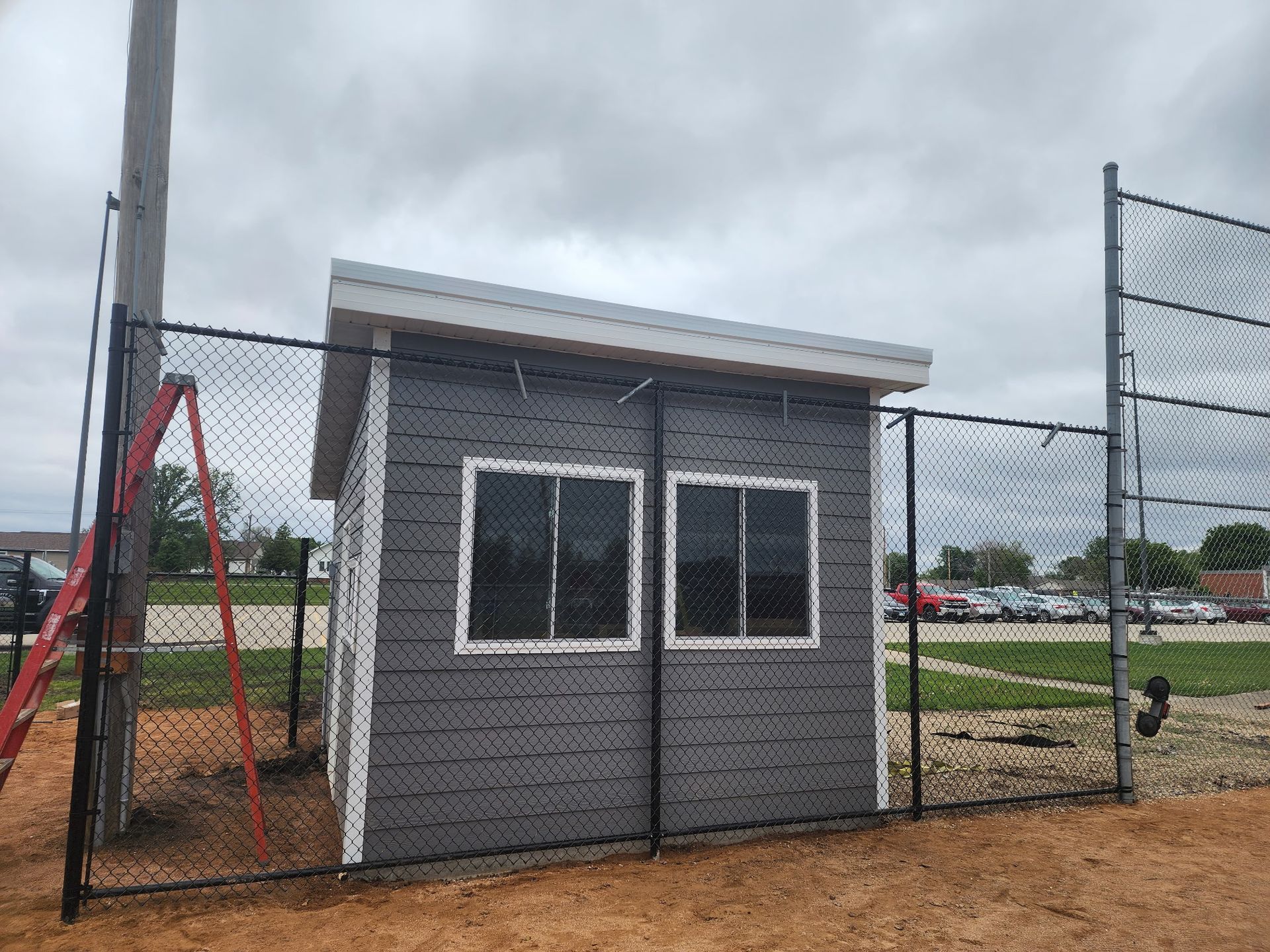 Small gray guard booth with two windows beside a chain-link fence on a cloudy day
