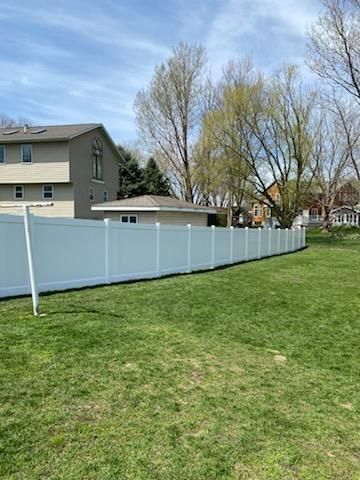 Backyard with green lawn and white vinyl fence beside houses under a partly cloudy sky