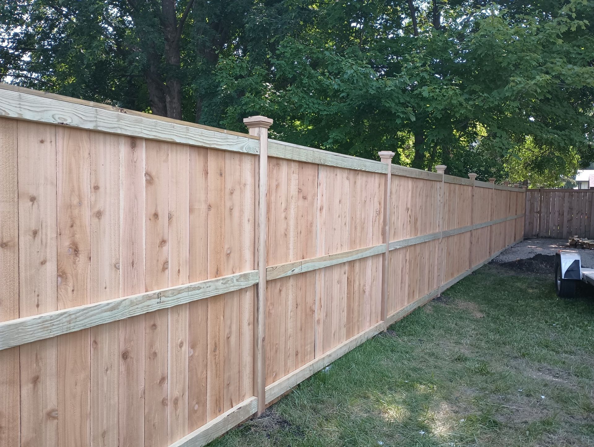 Wooden privacy fence running along a grassy backyard beside a patio area with outdoor furniture.