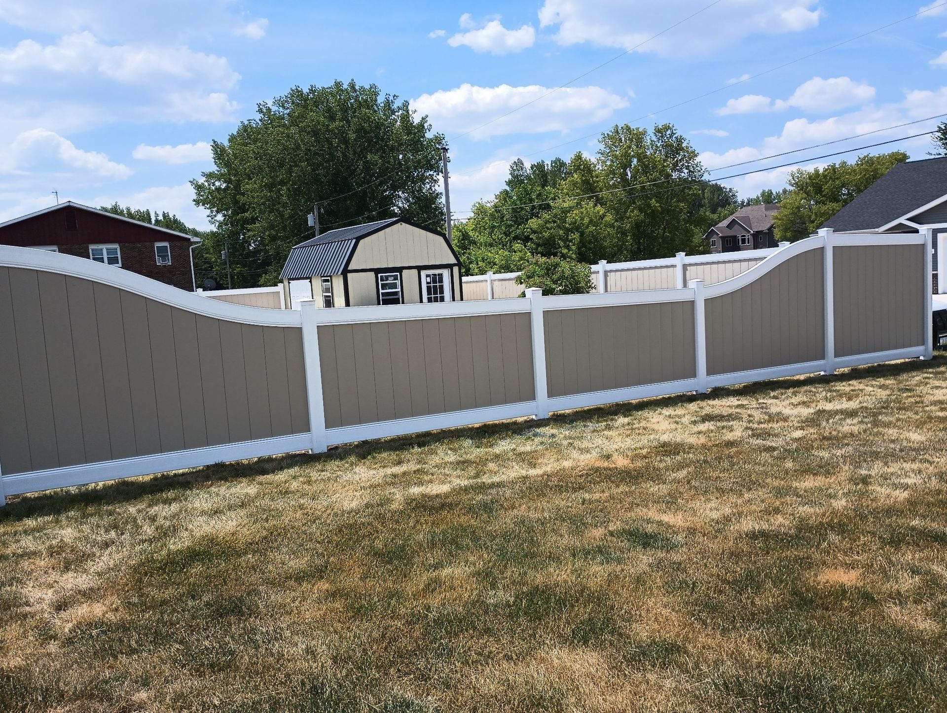 Backyard with tan-and-white fence, dry grass, and houses and trees in the background