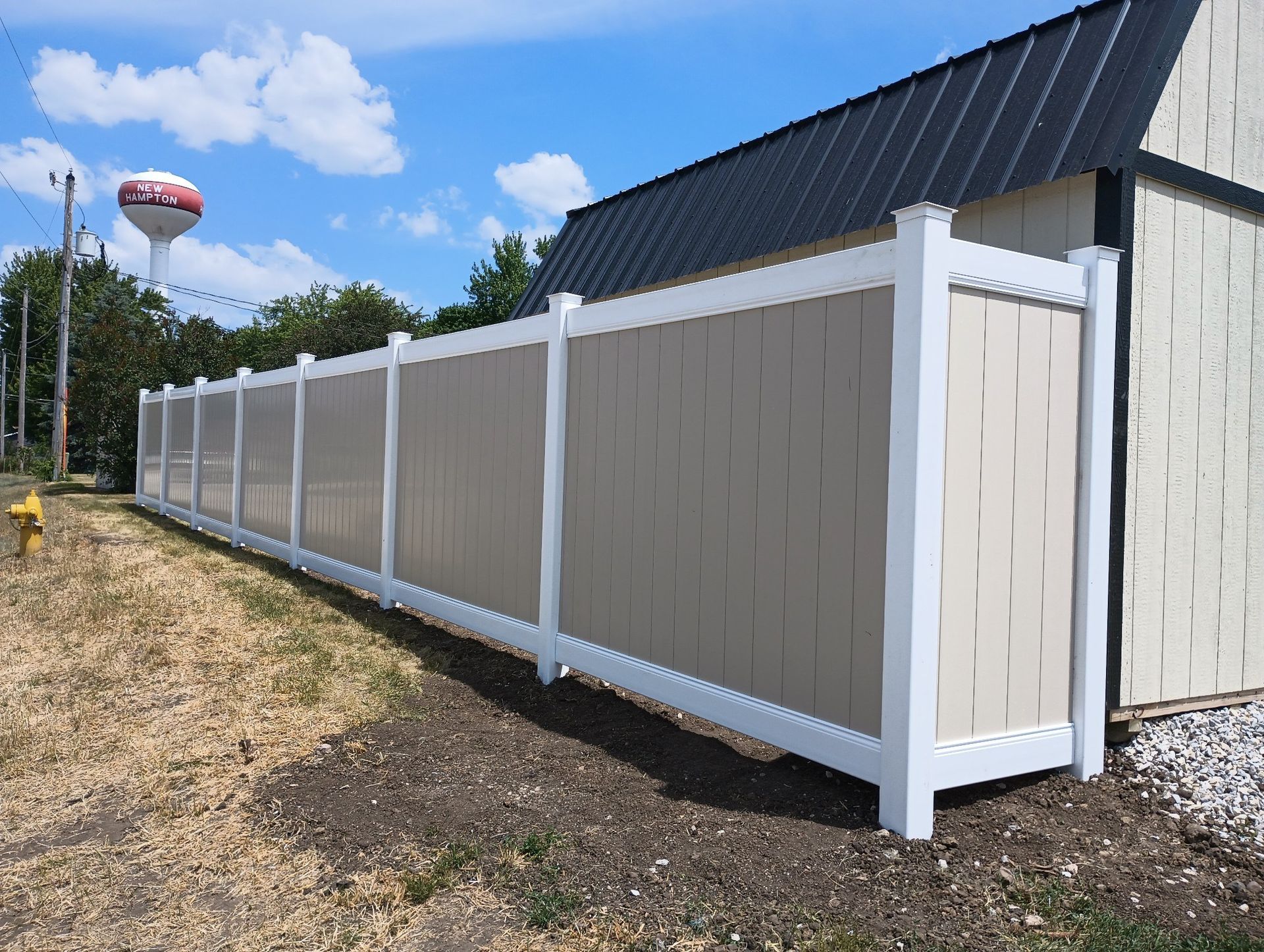 White vinyl fence along a driveway beside a tan house under a blue sky