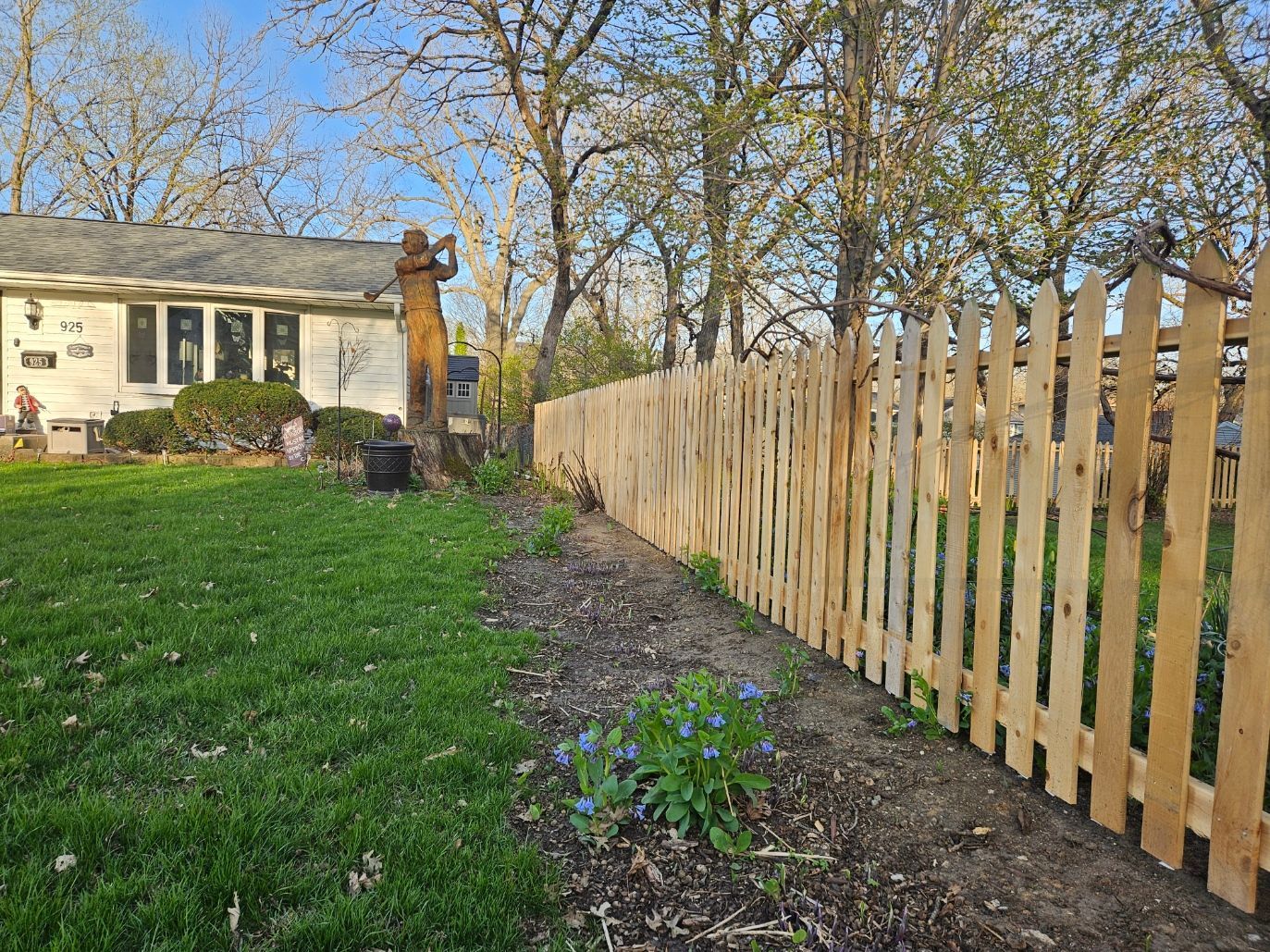 Wooden fence beside a grassy yard with a house and trees in the background
