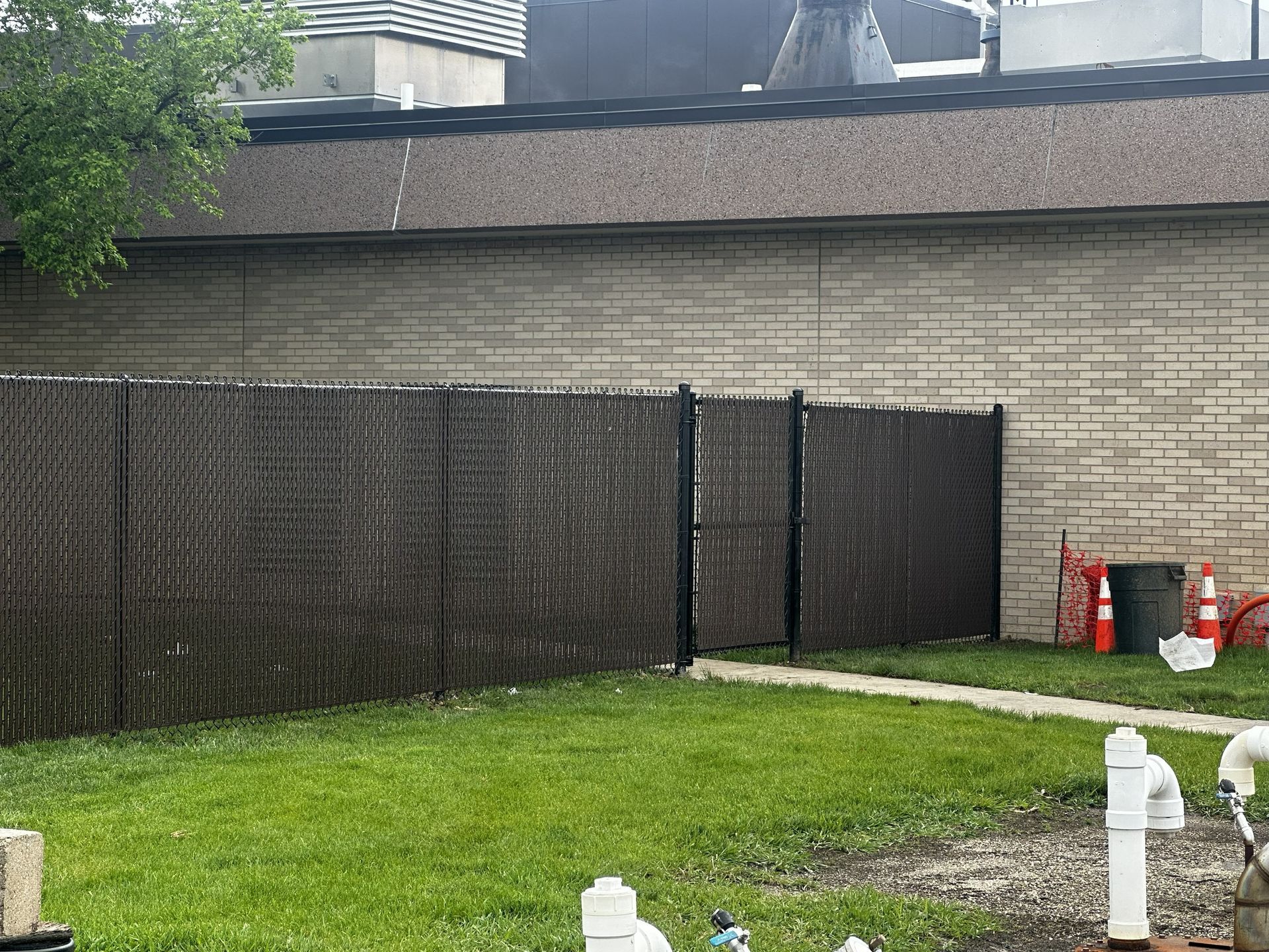 Backyard with green lawn, brown fence, and a small gravel path beside a house wall