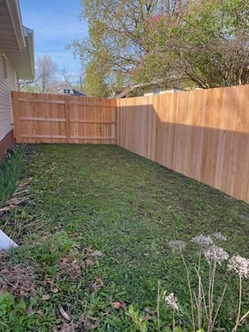 Narrow grassy backyard with a wooden fence and gate, beside a house under trees.