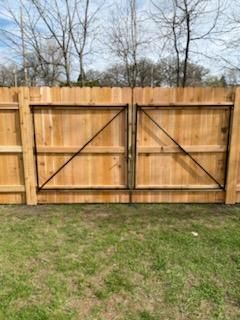 Wooden double gate in a backyard fence with grass in front and bare trees behind.
