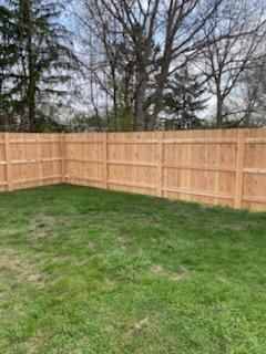 Empty grassy backyard corner with a wooden privacy fence and trees beyond it