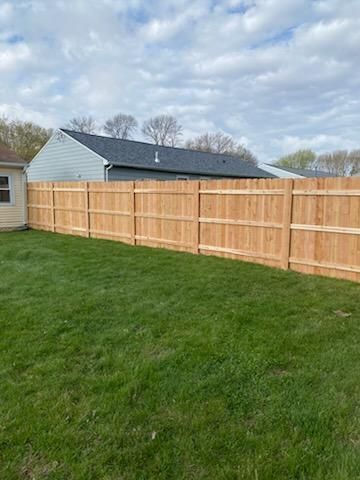 Backyard with green lawn and a long wooden privacy fence under a cloudy sky