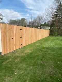 Wooden privacy fence along a grassy yard under a partly cloudy sky